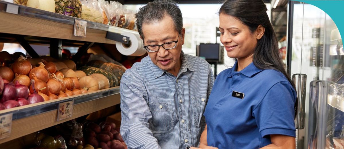 2 people in a grocery store. One is an older man and the other is a woman in a uniform with a name tag.