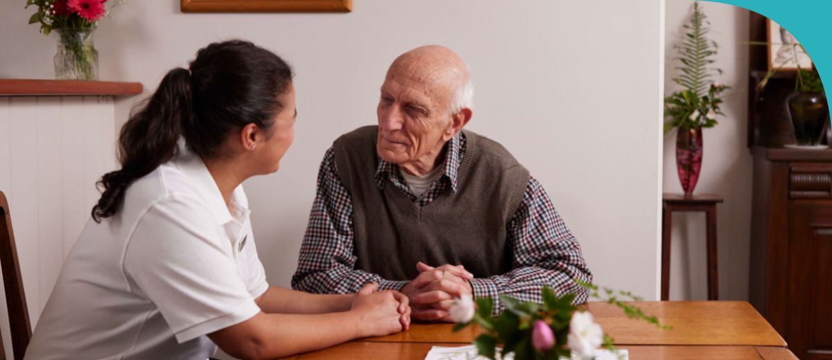 An older man and a woman sit at a table talking face to face