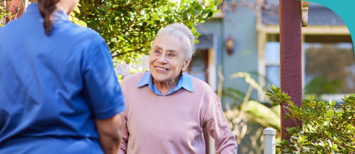 An older lady in her garden smiling and looking at a younger lady whose back is to the camera