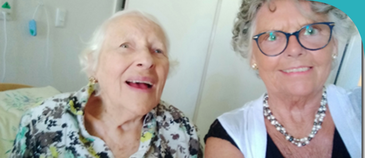 A woman visiting an older lady at an aged care facility. They are both smiling at the camera