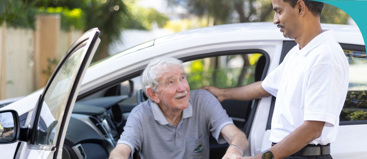 A man helps an older man out of the passenger seat of a car.