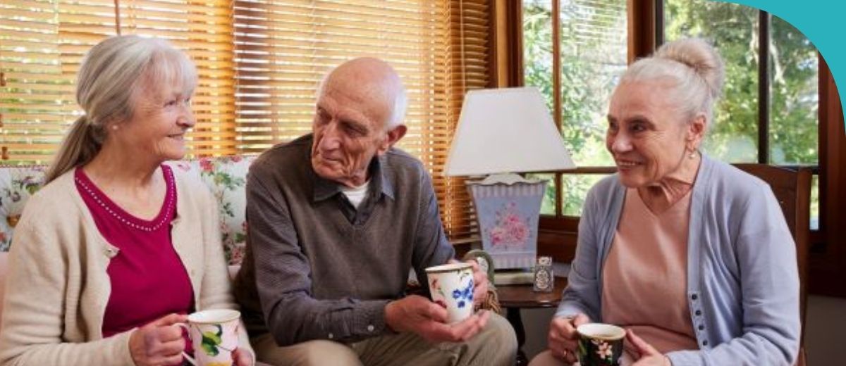 Two older ladies and an older man chatting and having a cup of tea